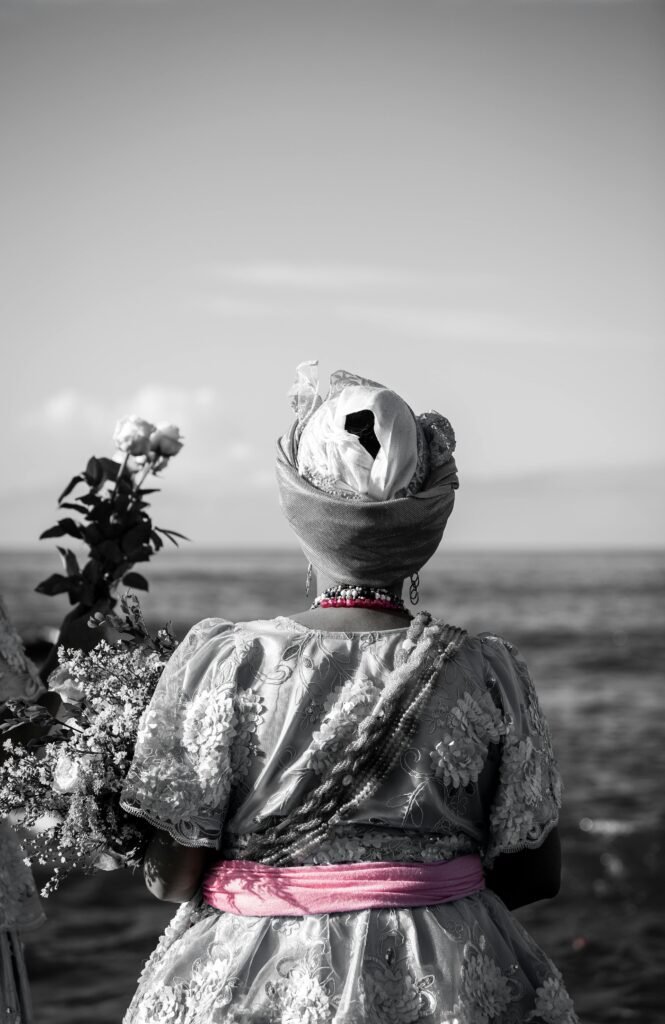 A Baiana woman in traditional attire stands by the ocean in Salvador, Brazil. Grayscale with pink details.